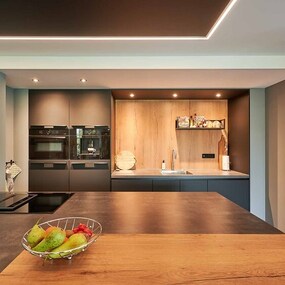 Moderne Küche mit Kochinsel, Obstschale, Einbaugeräten und stilvoller Beleuchtung.