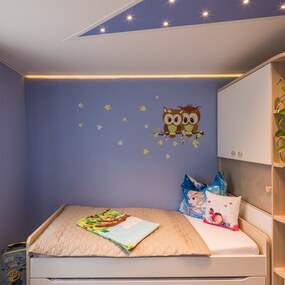 Modern eingerichtetes Kinderzimmer mit gemütlichem Bett, Eulen-Wanddeko und Pflanzen.